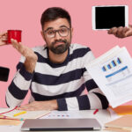 brunet-man-sitting-desk-surrounded-with-gadgets-papers