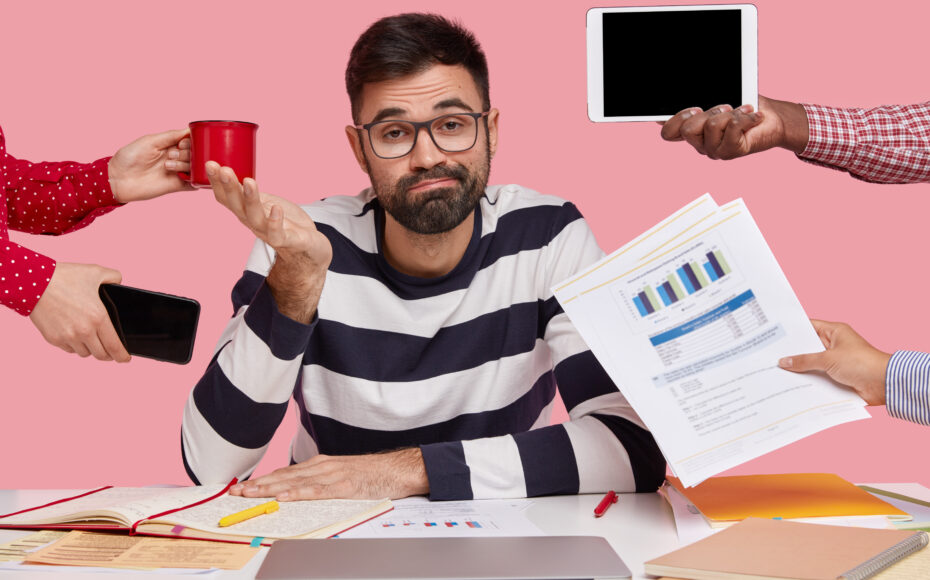 brunet-man-sitting-desk-surrounded-with-gadgets-papers