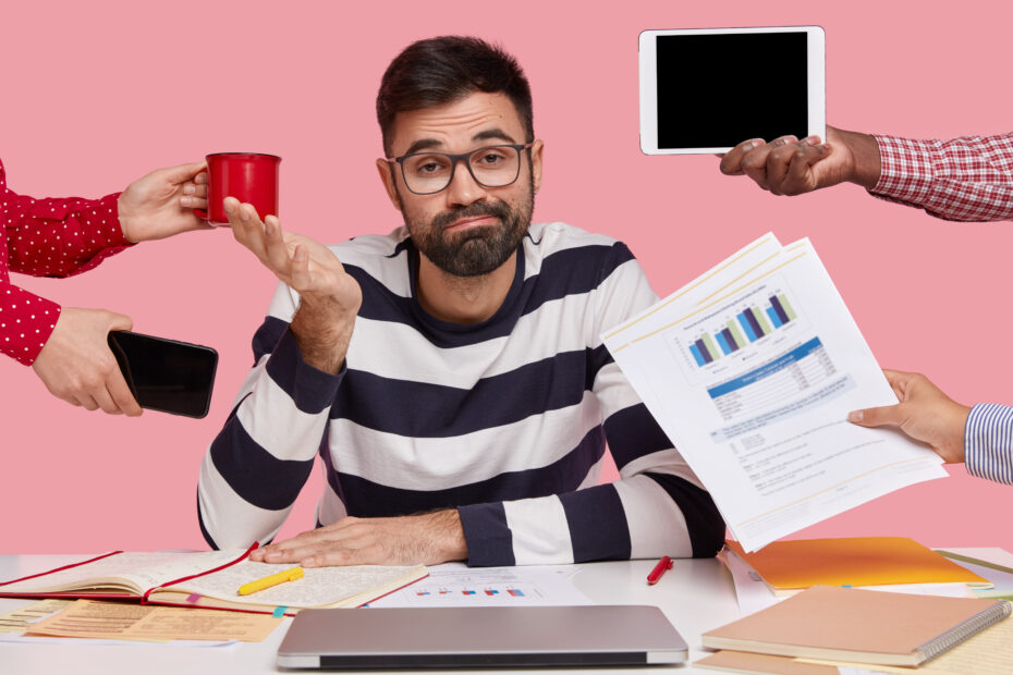 brunet-man-sitting-desk-surrounded-with-gadgets-papers