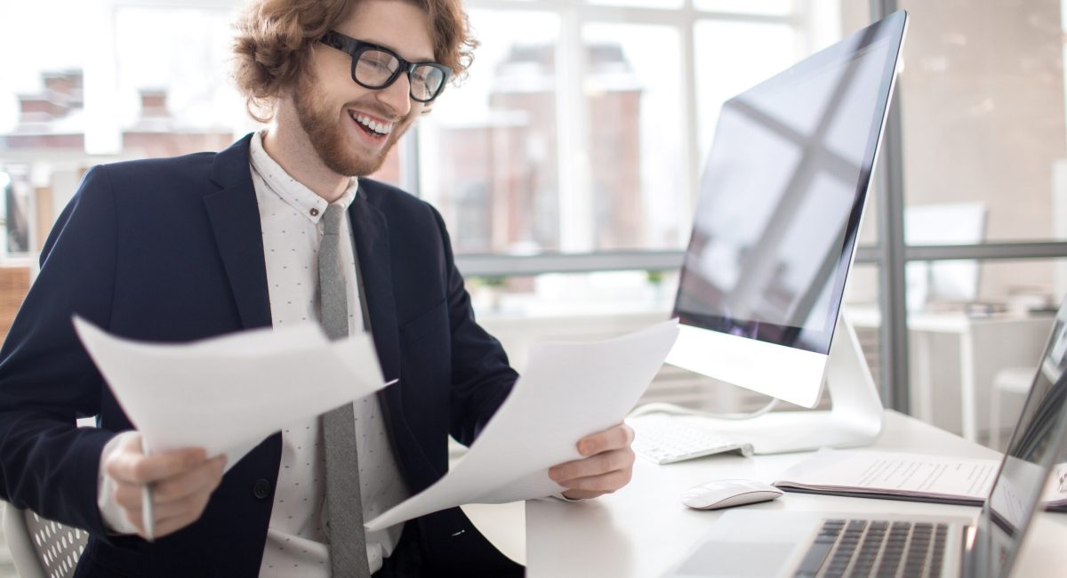 Happy young financier reading documents or new contracts in office